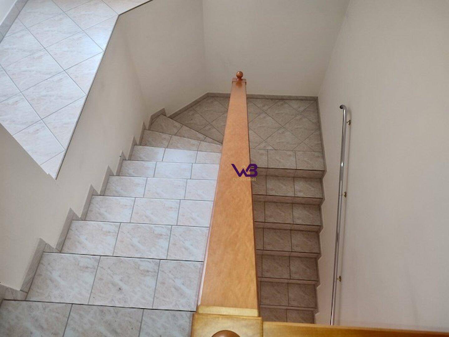Treppenhaus mit gefliesten Stufen und Holzgeländer, das die Stockwerke verbindet.