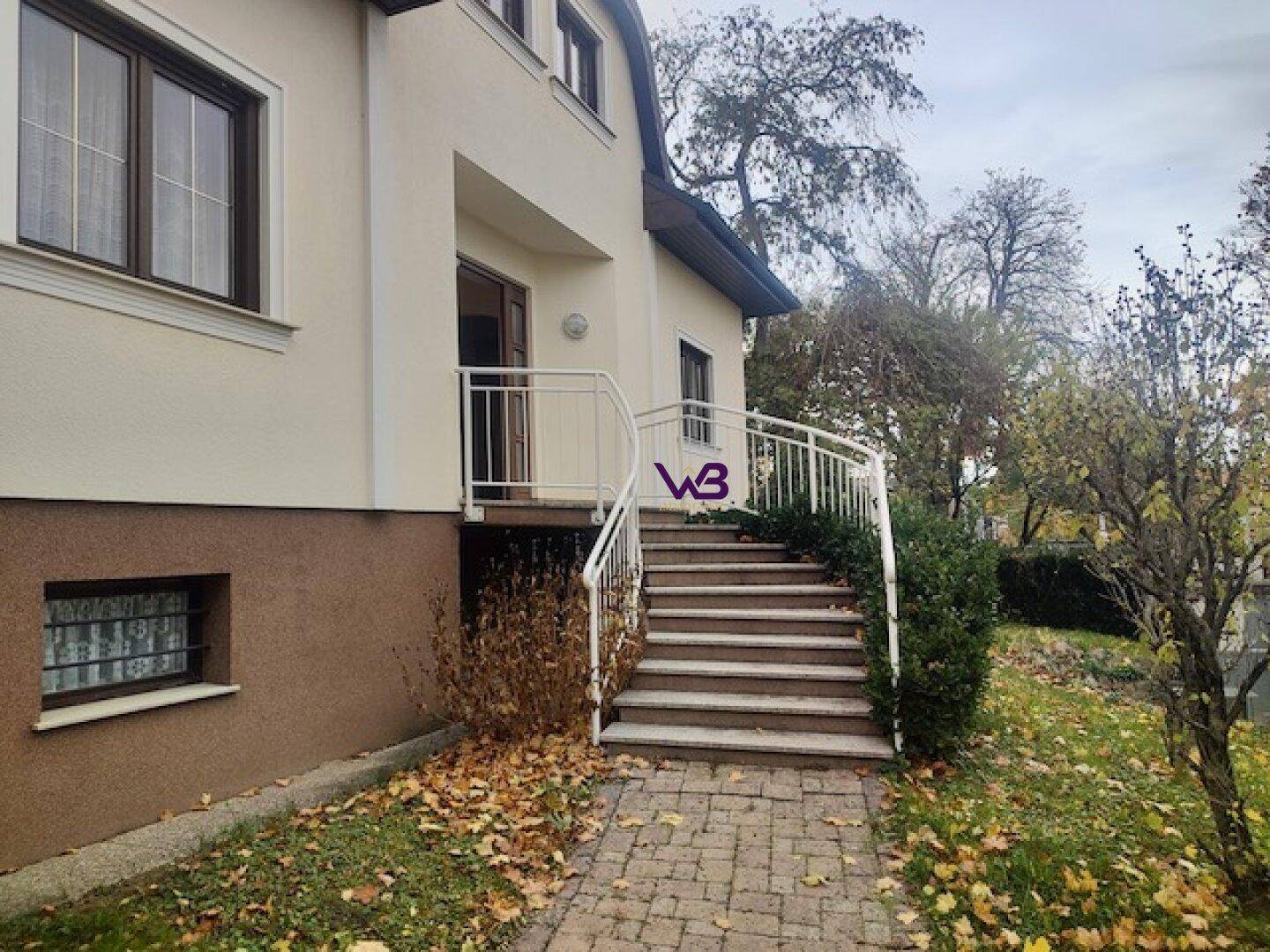 Eingangsbereich des Hauses mit Treppe und Geländer, umgeben von herbstlichem Laub.