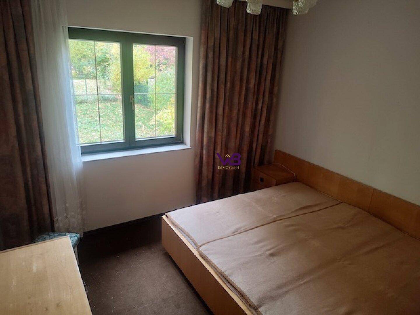 Schlafzimmer mit Bett, Nachttisch und Fenster mit Blick ins Grüne.