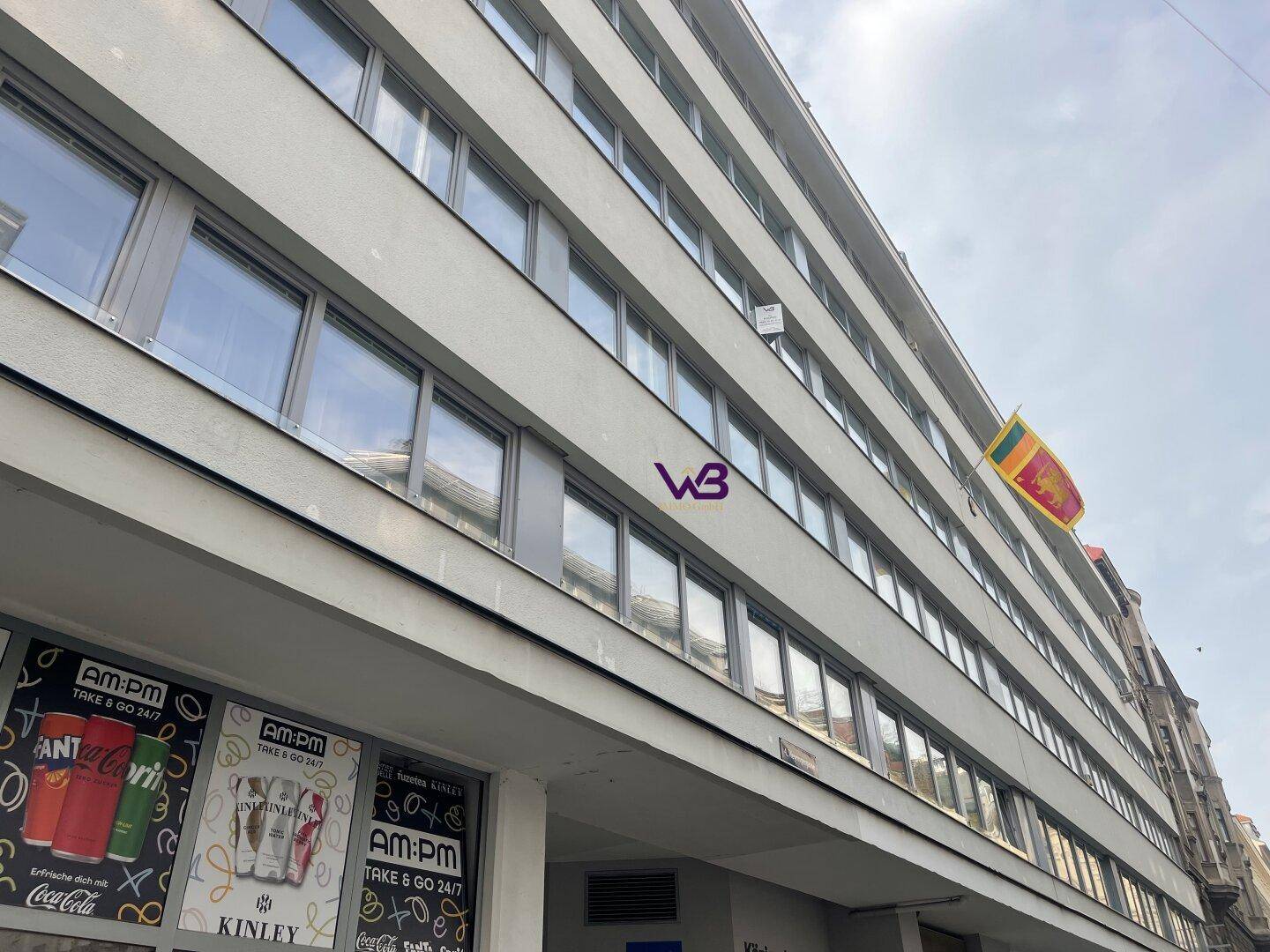 Nahaufnahme der Fassade eines modernen Gebäudes mit Geschäften im Erdgeschoss und vielen Fenstern.