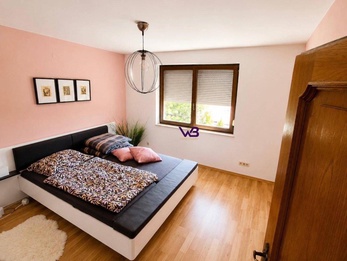 Schlafzimmer mit Holzboden, Doppelbett und rosa Akzentwand, bietet eine ruhige Atmosphäre.