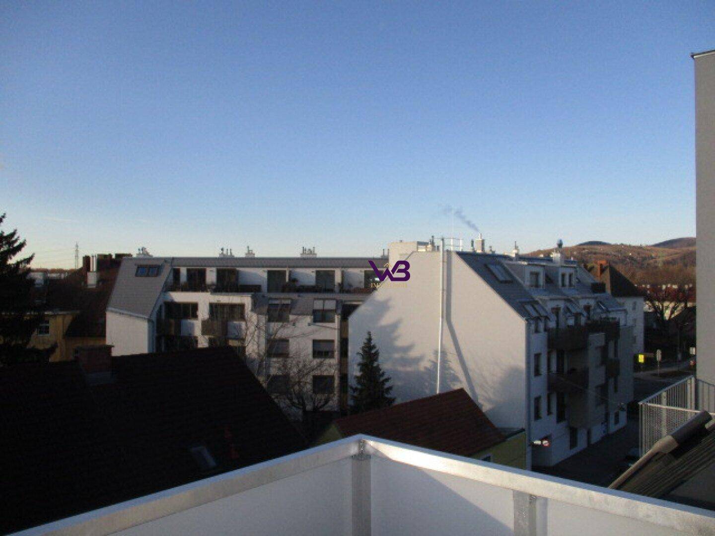 Weitläufiger Blick über städtische Dächer und grüne Hügel am Horizont unter klarem Himmel.