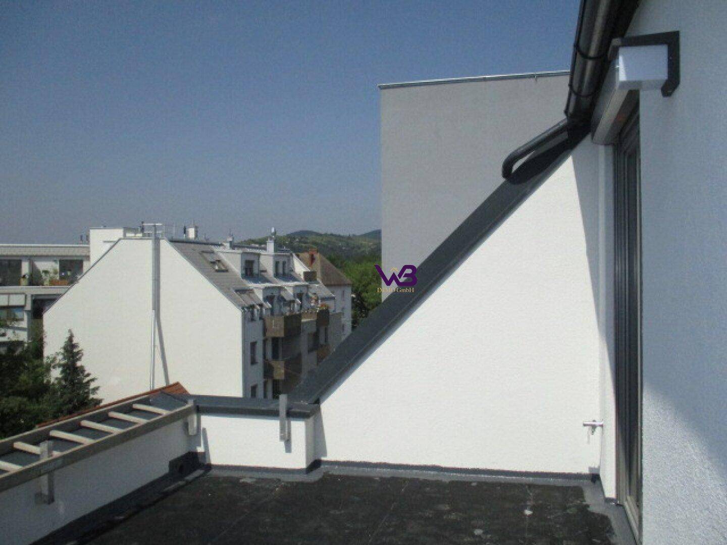 Flachdachbereich eines Gebäudes mit Blick auf die umliegende Bebauung und ferne Hügel.
