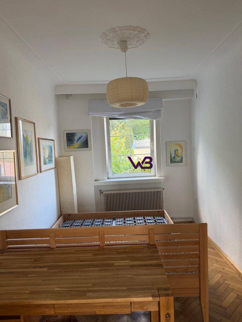 Schlafzimmer mit Holzbett, Fischgrätparkett und einem Fenster mit Blick ins Grüne.