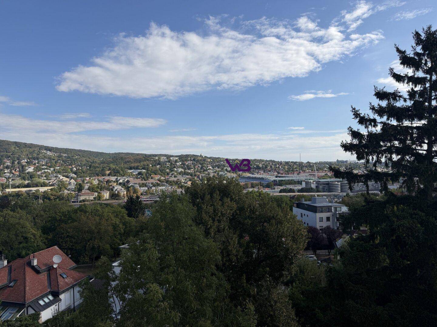 Panoramablick über eine grüne Stadtlandschaft mit bewaldeten Hügeln am Horizont.