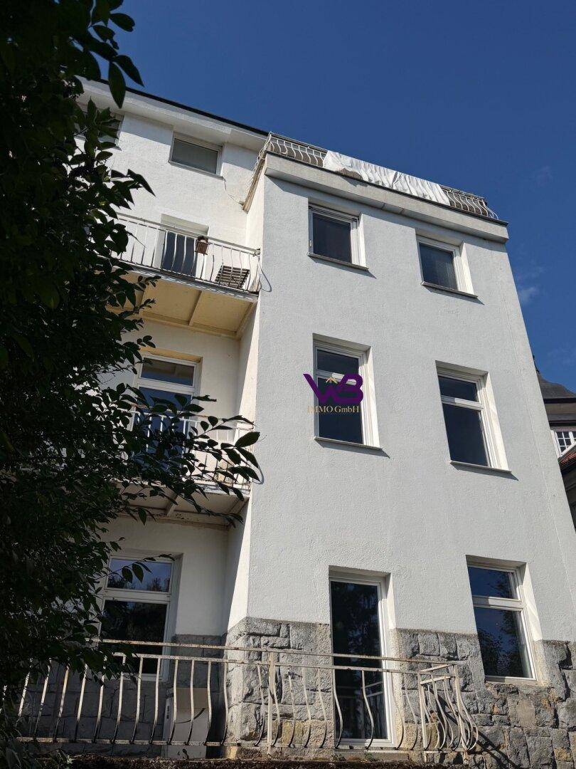 Seitenansicht des Gebäudes mit mehreren Balkonen und einer steinverkleideten unteren Etage.