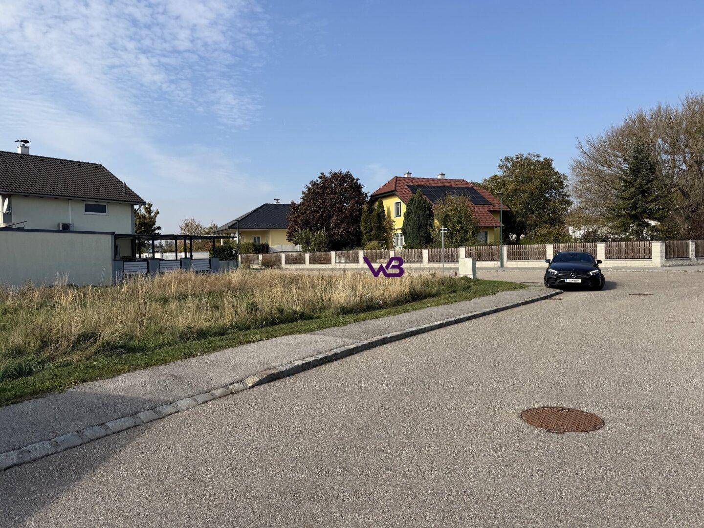 Weitläufiges Grundstück an einer ruhigen Straße mit umliegenden Wohnhäusern unter blauem Himmel.