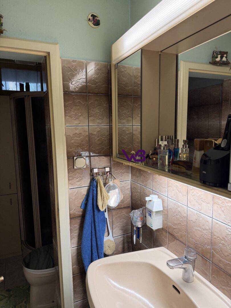 Kleines Badezimmer mit Waschbecken, Spiegelschrank und braunen Wandfliesen.