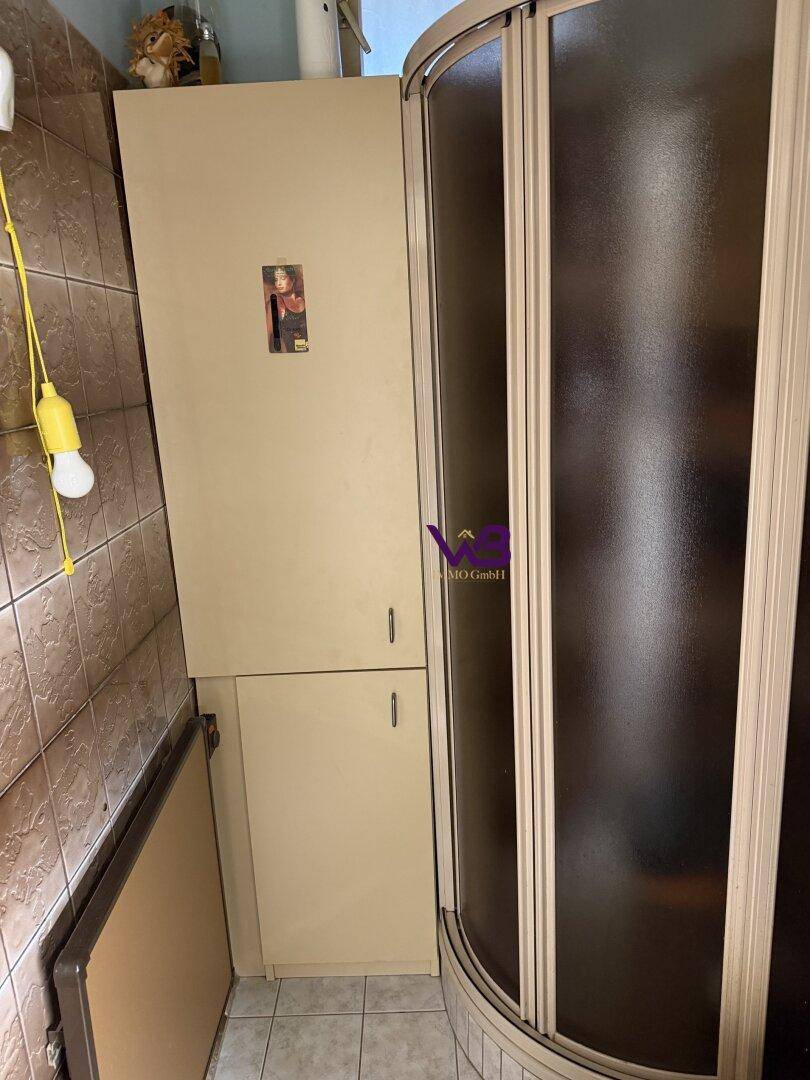 Duschbereich mit abgerundeter Duschkabine und einem schmalen Hochschrank.