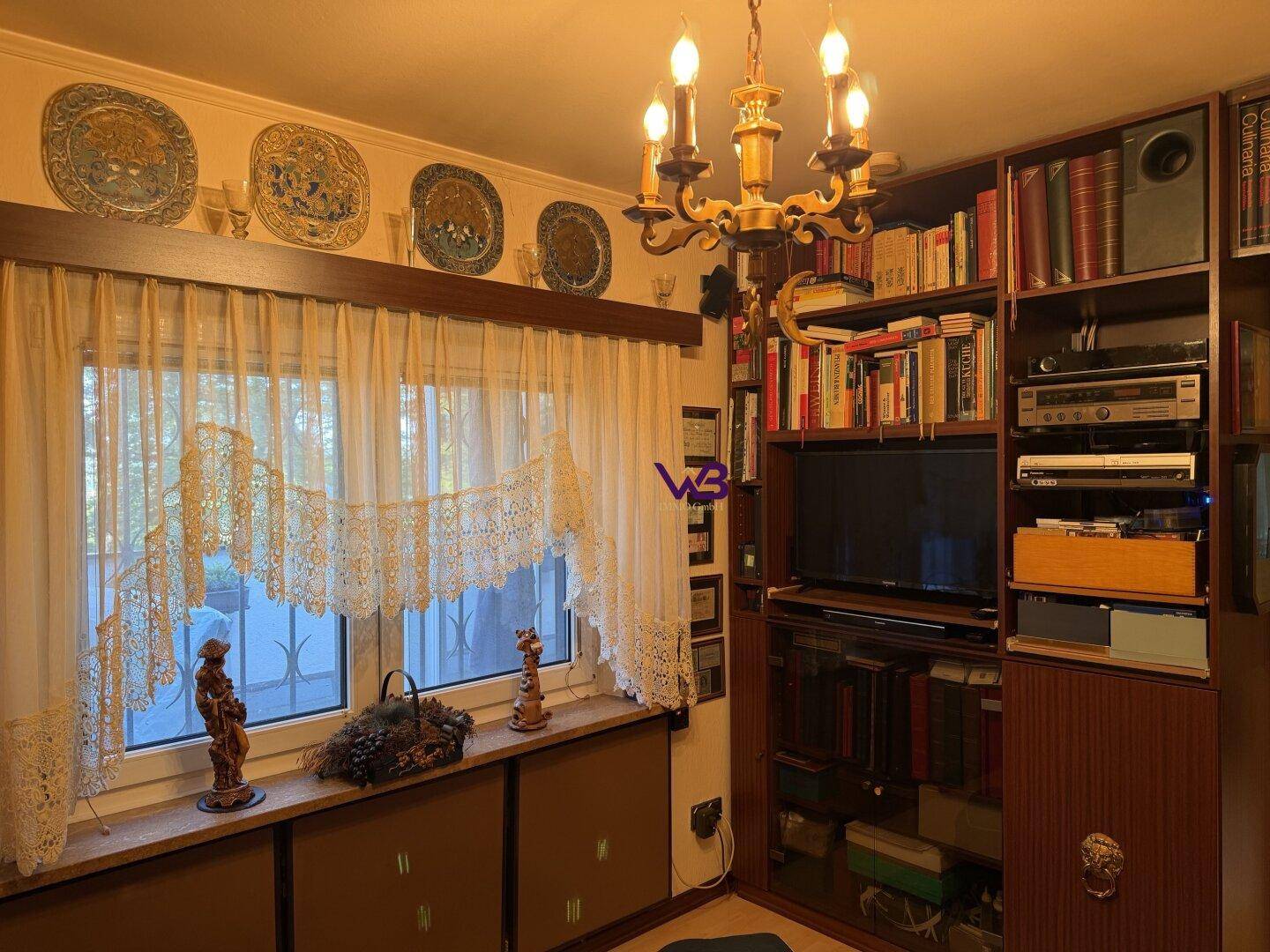 Wohnzimmer mit großem Fenster, Bücherregal und traditionellen Dekorationselementen.