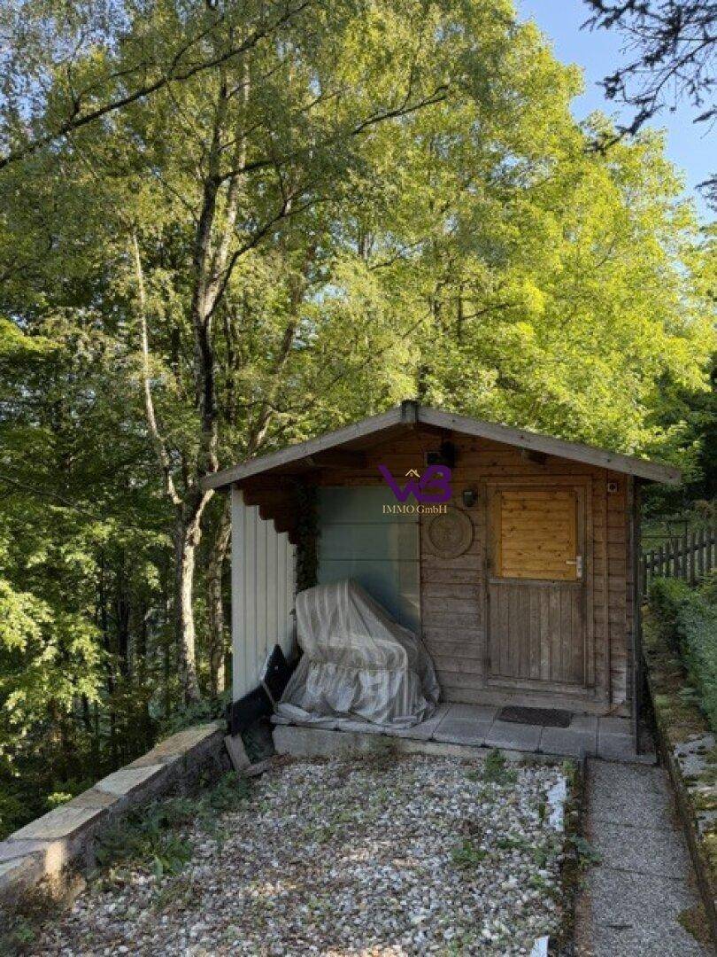 Rustikaler Gartenschuppen aus Holz, umgeben von Bäumen und Grünflächen.