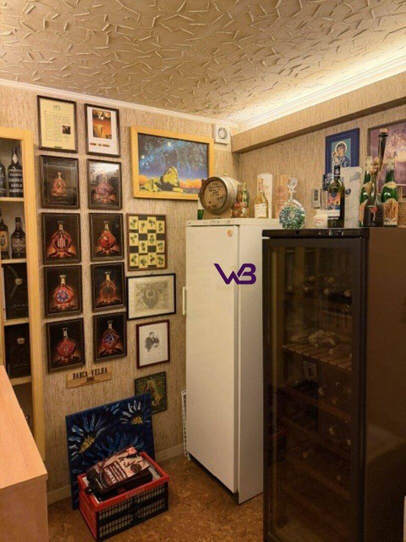 Lagerraum mit Kühlschrank, Weinkühler und vielen gerahmten Bildern an der Wand.