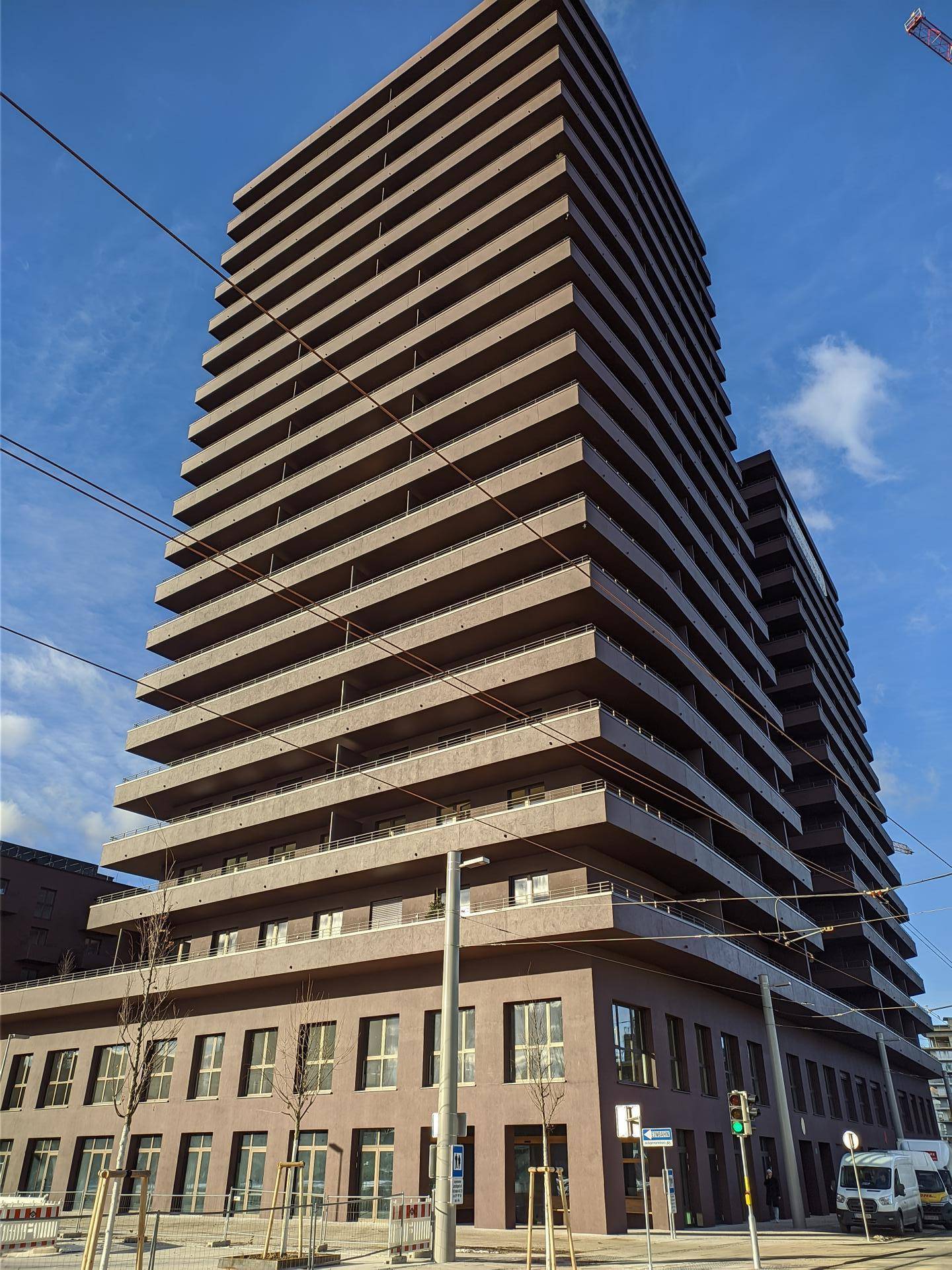 Hohes, modernes Wohngebäude mit vielen Balkonen und einer markanten Fassade unter blauem Himmel.