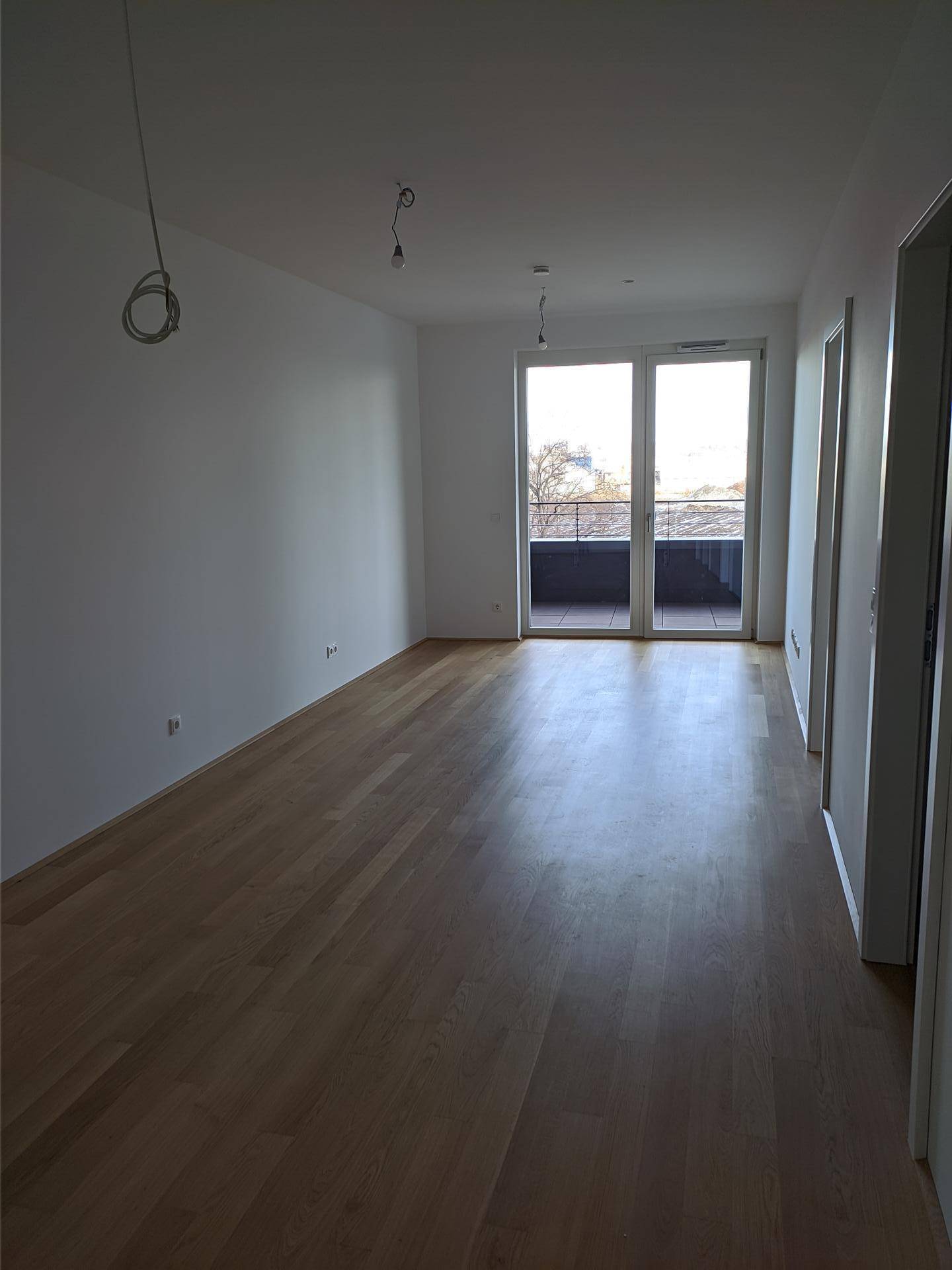 Geräumiger, heller Raum mit Parkettboden und großen Fenstern, die viel Tageslicht hereinlassen.