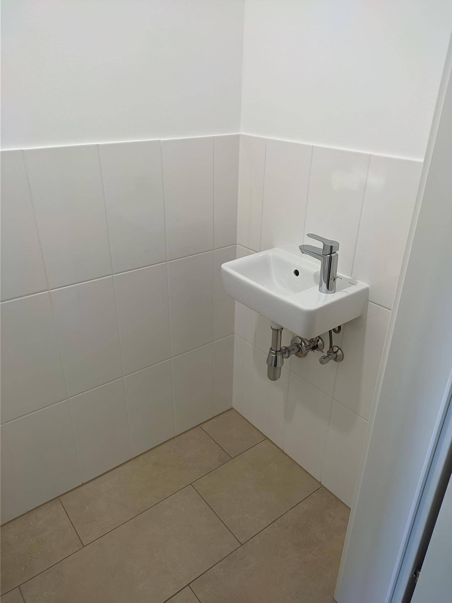 Kleines, gefliestes Gäste-WC mit modernem Waschbecken und hellen Fliesen.