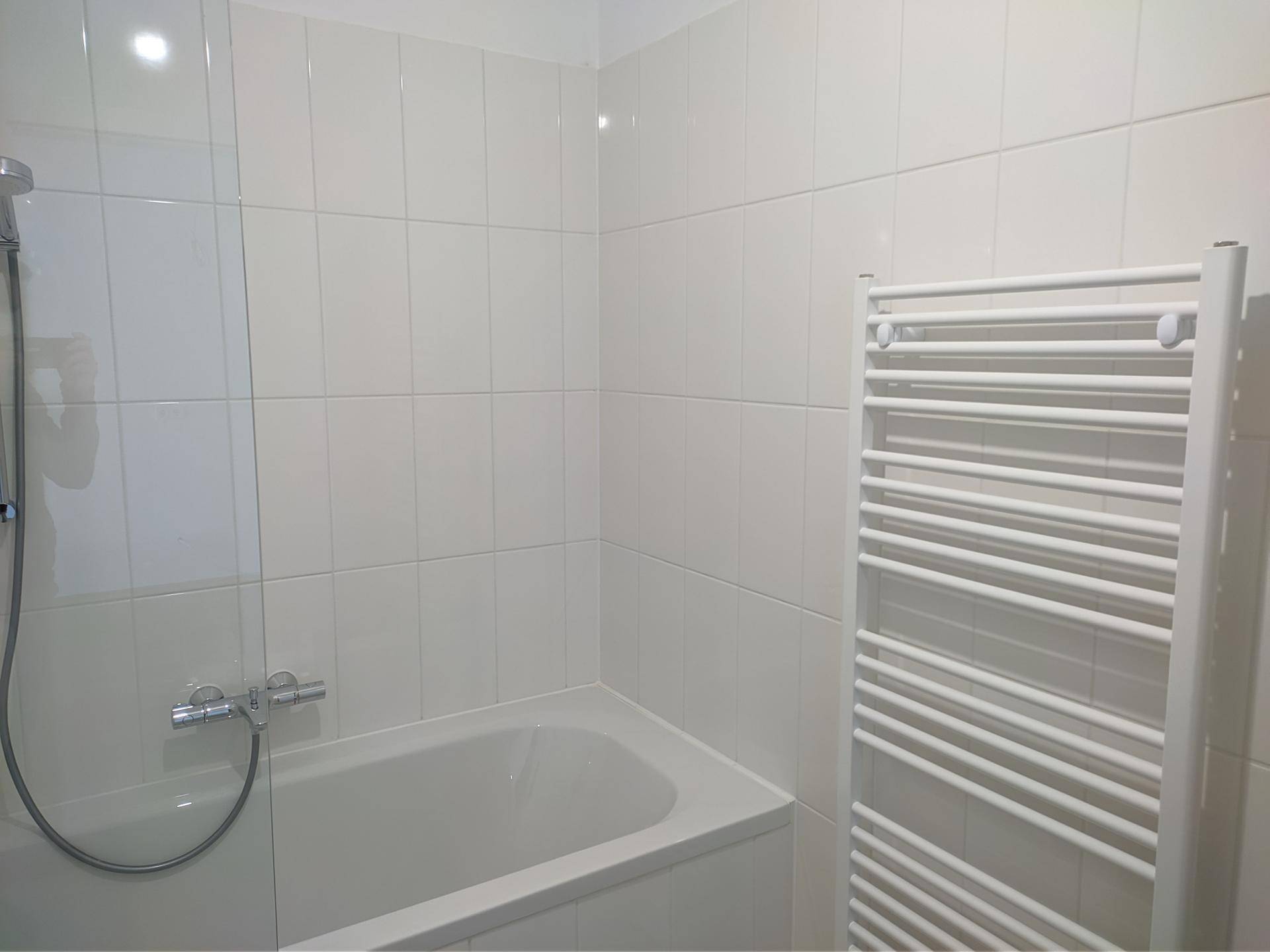 Helles Badezimmer mit Badewanne, Duscharmatur und beheiztem Handtuchhalter.
