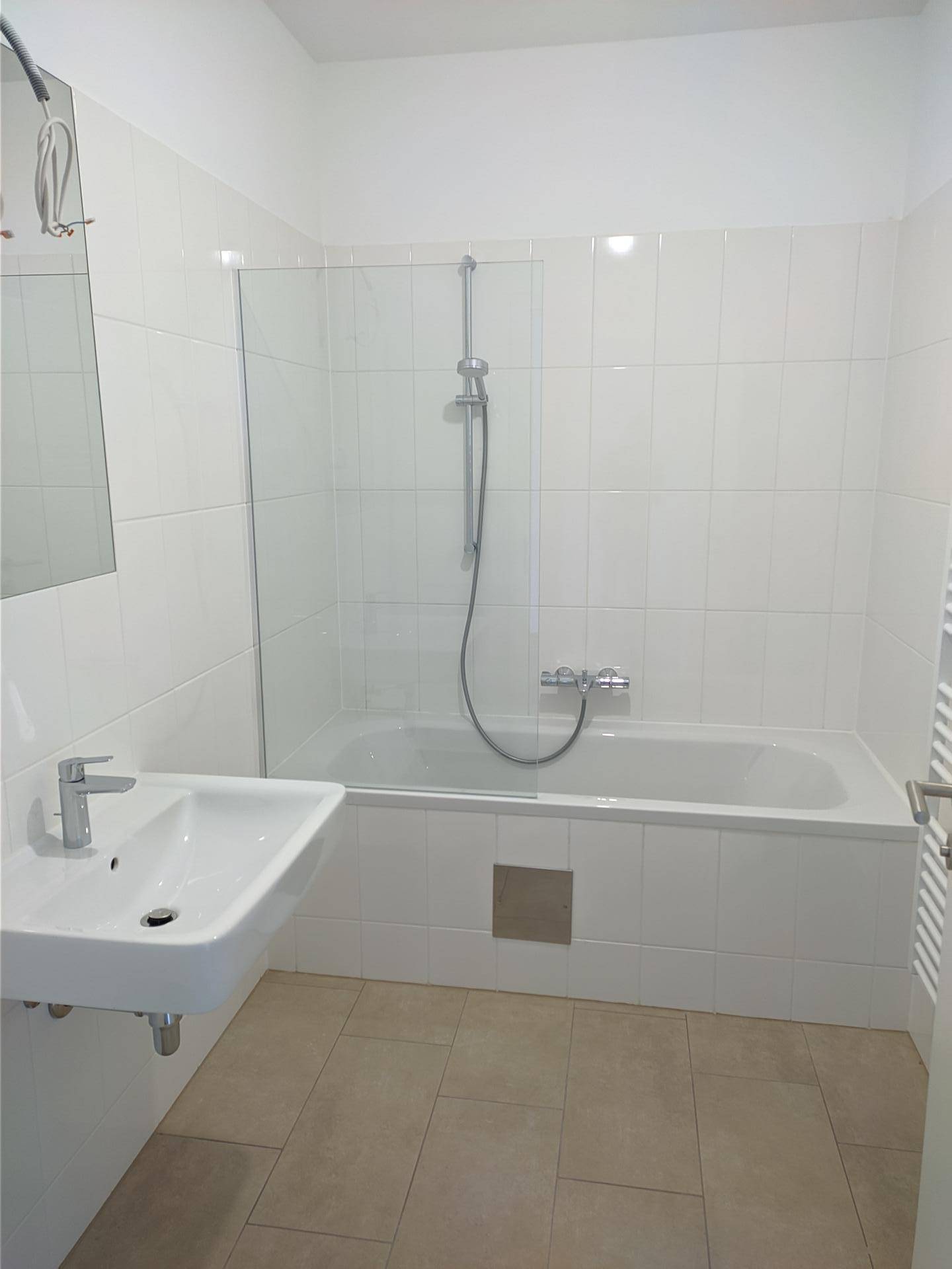 Modernes Badezimmer mit Waschbecken, Badewanne mit Duschfunktion und hellen Fliesen.