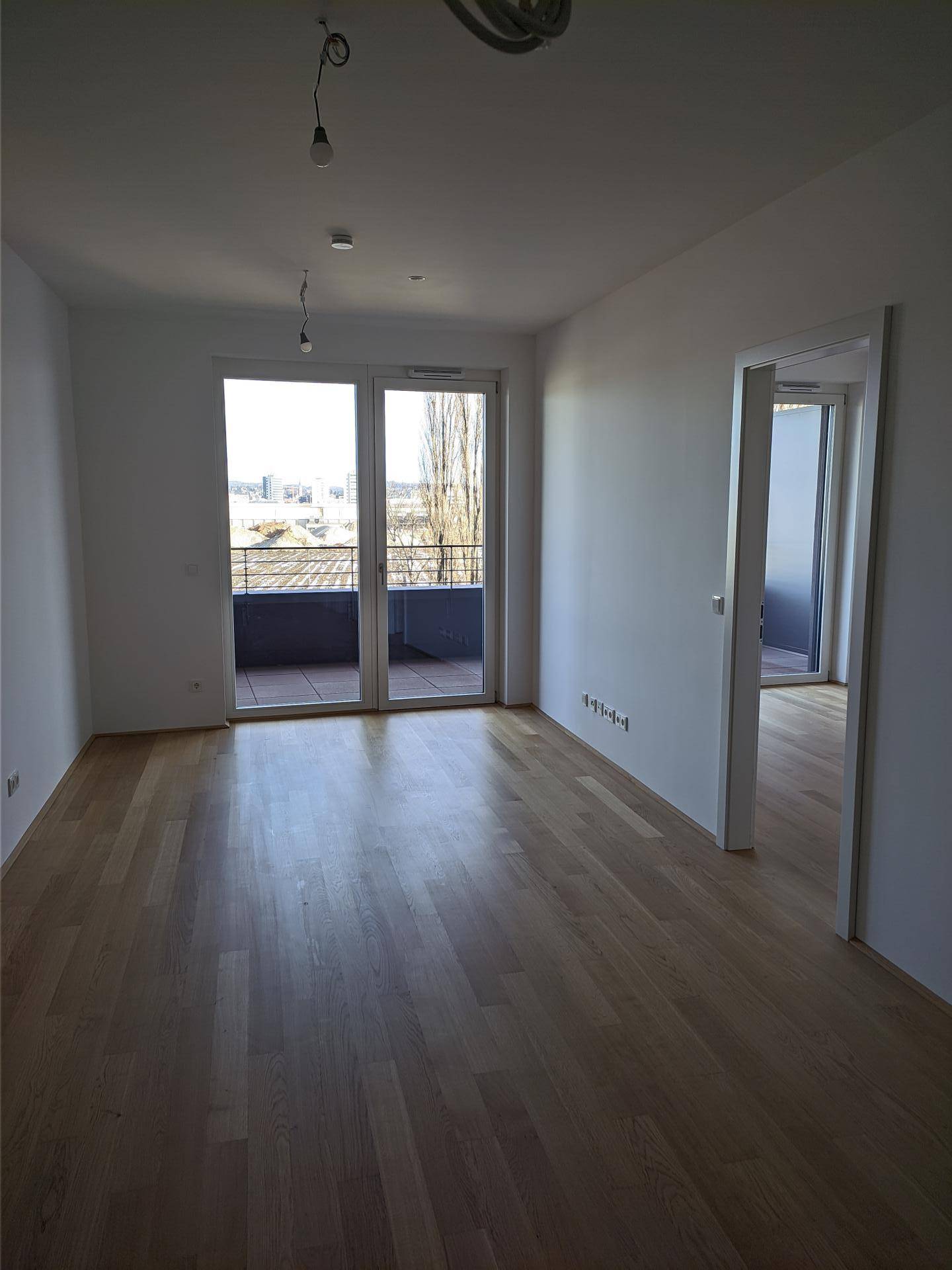 Heller, unmöblierter Raum mit Holzboden und Zugang zu einem Balkon, ideal für Wohnzwecke.