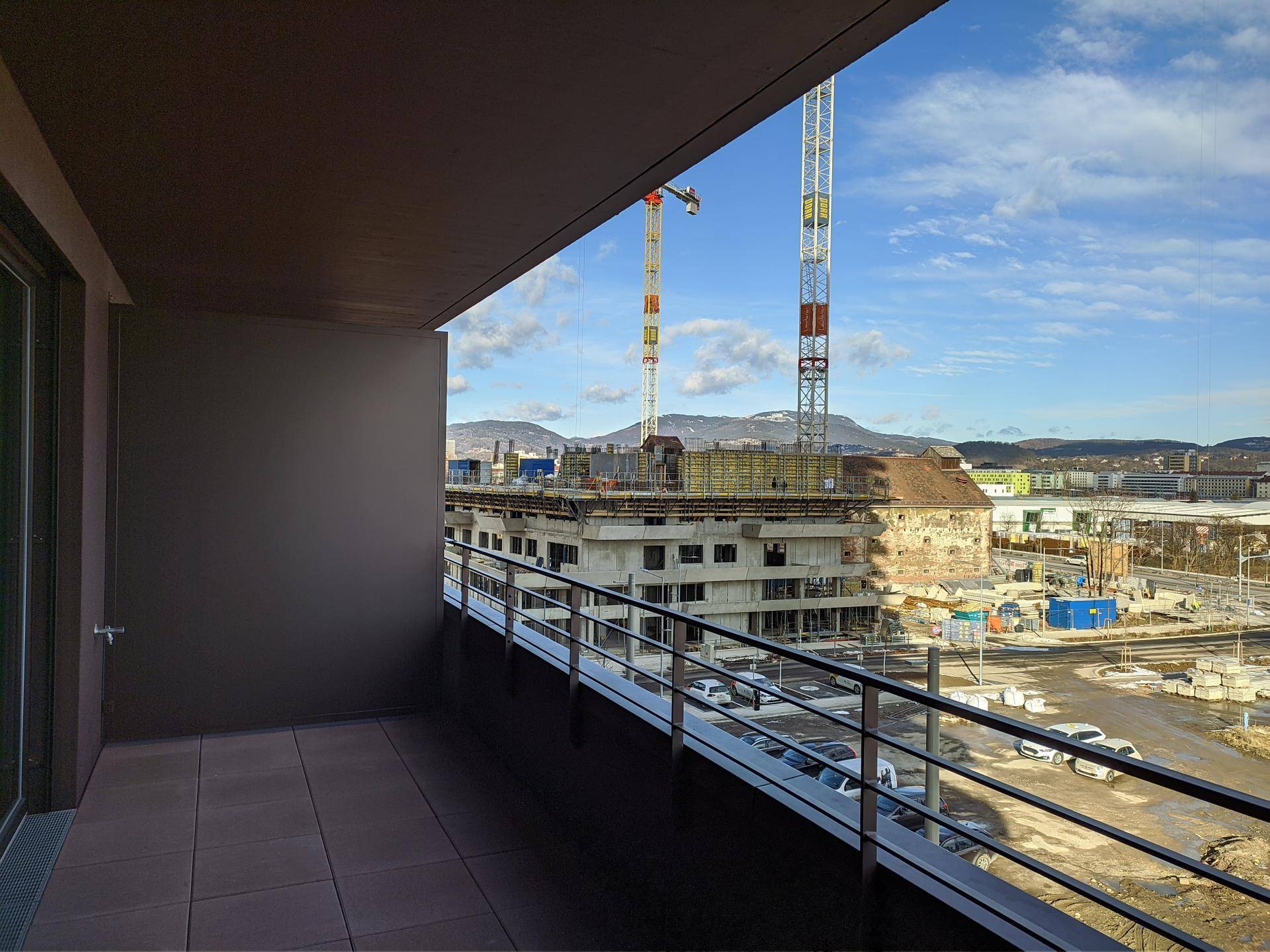 Geräumiger Balkon mit Metallgeländer und weitem Blick über die Stadt und Baustellen.