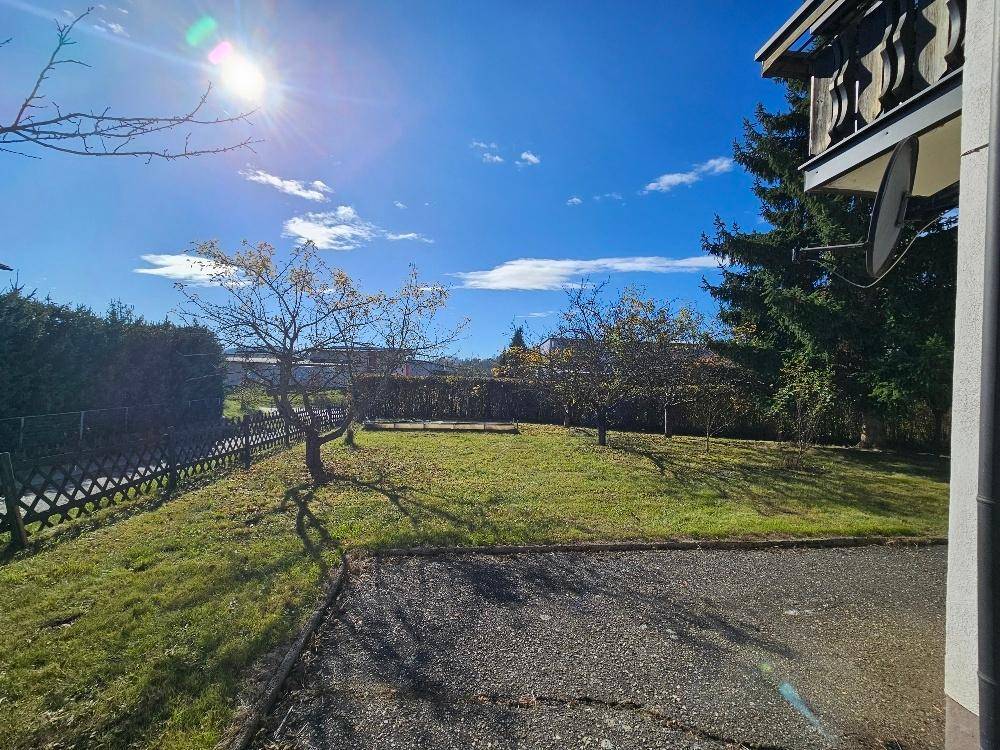 Sonniger Gartenbereich mit Rasen, Bäumen und Blick auf die umliegende Landschaft.