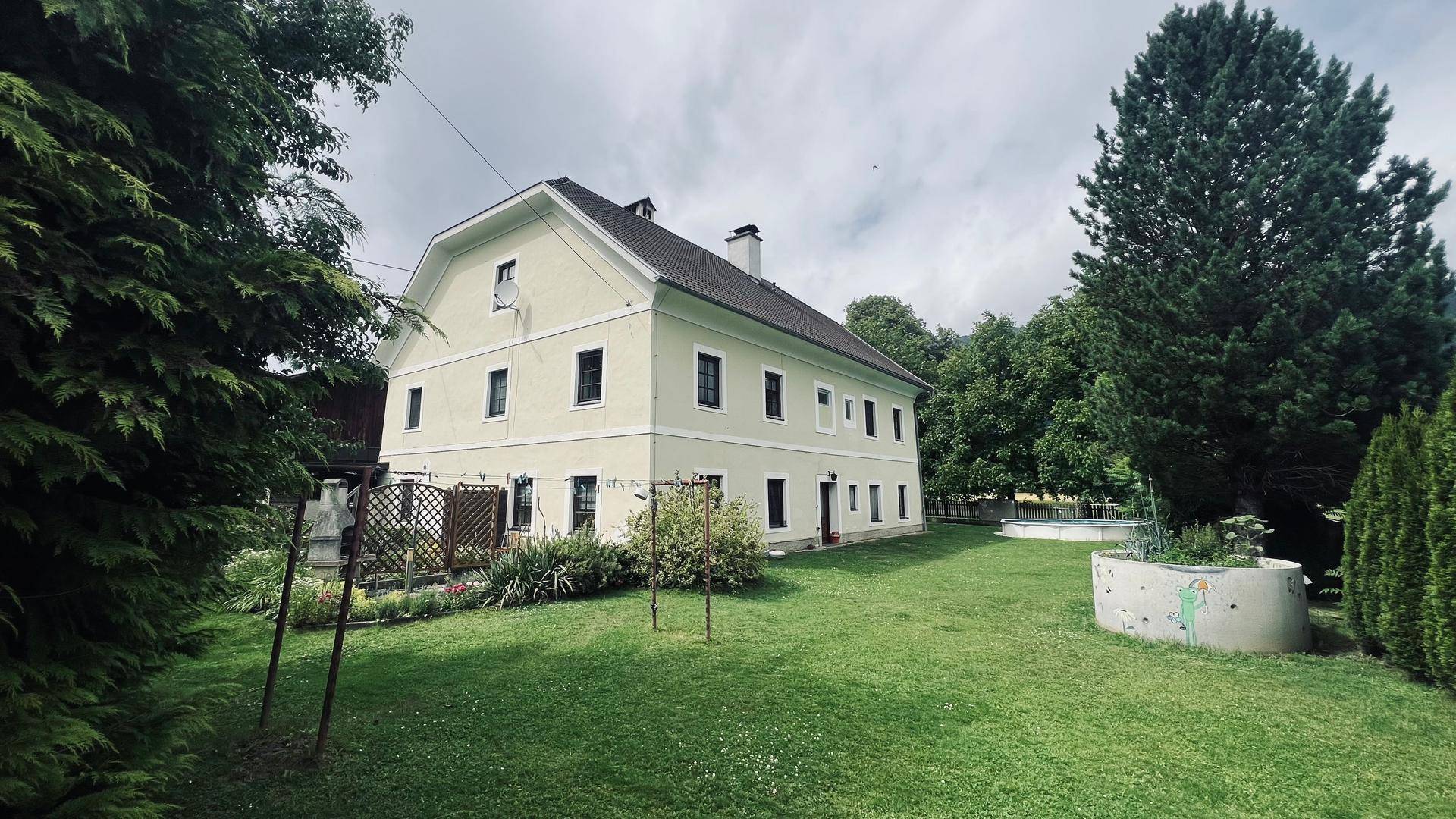 Großzügiger Gartenbereich mit Rasenfläche und einem traditionellen Gebäude im Hintergrund unter bewölktem Himmel.