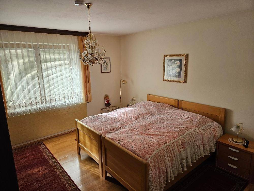 Helles Schlafzimmer mit Doppelbett, Parkettboden und Fenster mit Vorhängen.