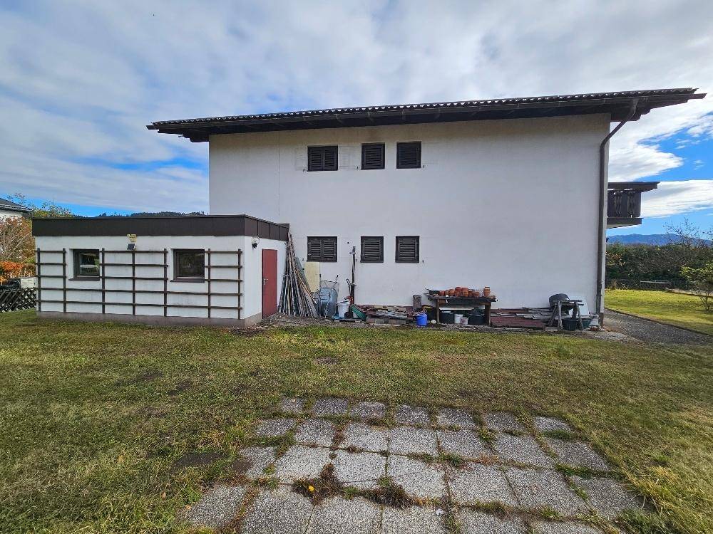 Rückseite des Hauses mit großem Garten, Nebengebäude und gepflastertem Bereich.