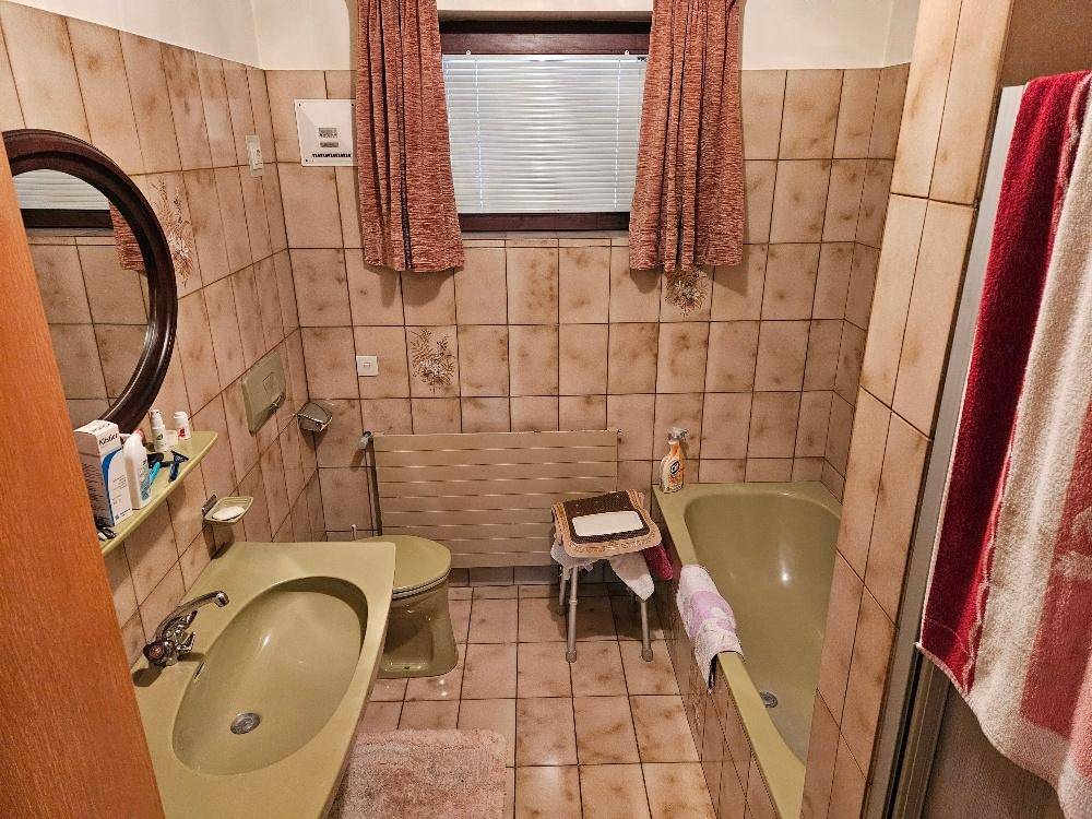 Badezimmer mit beigefarbenen Fliesen, Badewanne und Fenster, im Stil der 80er Jahre.