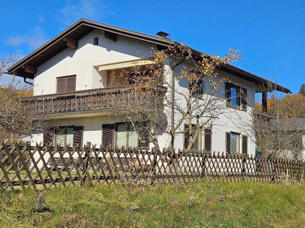Einfamilienhaus mit traditionellen Fensterläden und Holzbalkon, eingebettet in eine grüne Landschaft.