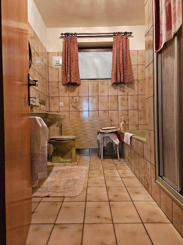 Badezimmer mit beigefarbenen Fliesen, Badewanne und Duschbereich, typisch für die 80er Jahre.