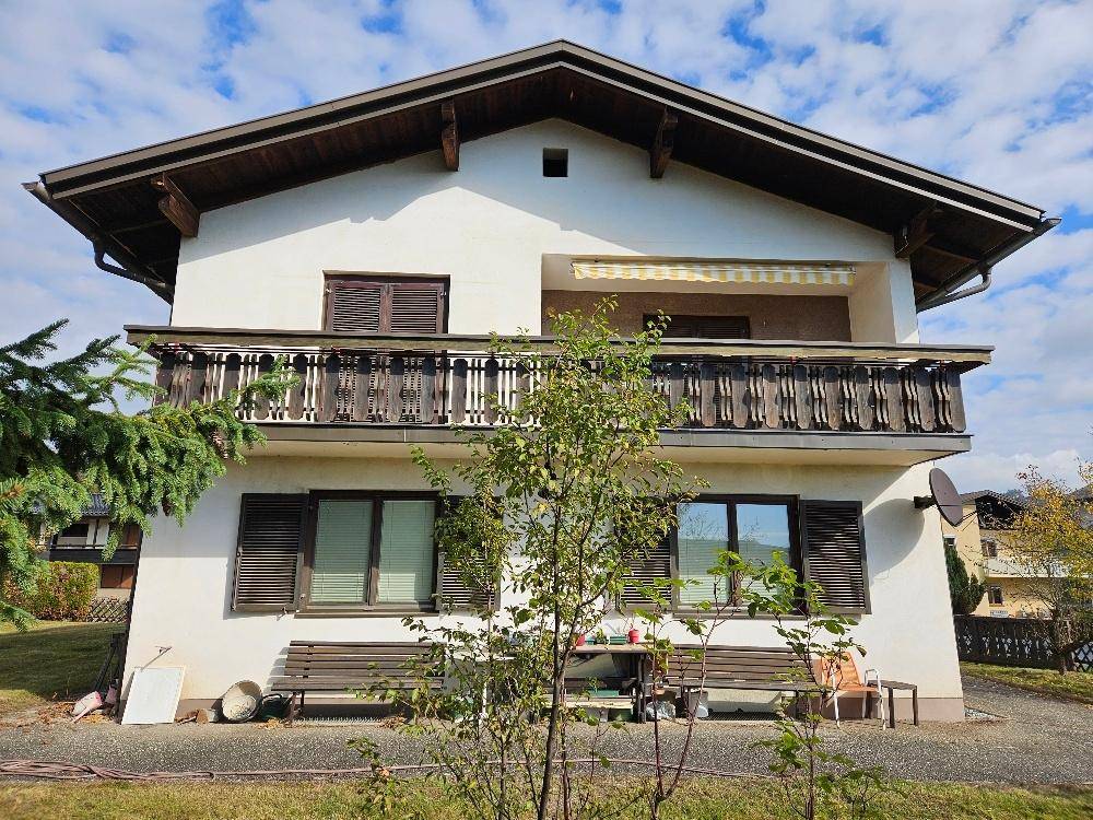 Vorderansicht des Hauses mit traditionellem Holzbalkon, Fensterläden und Markise über dem oberen Balkon.