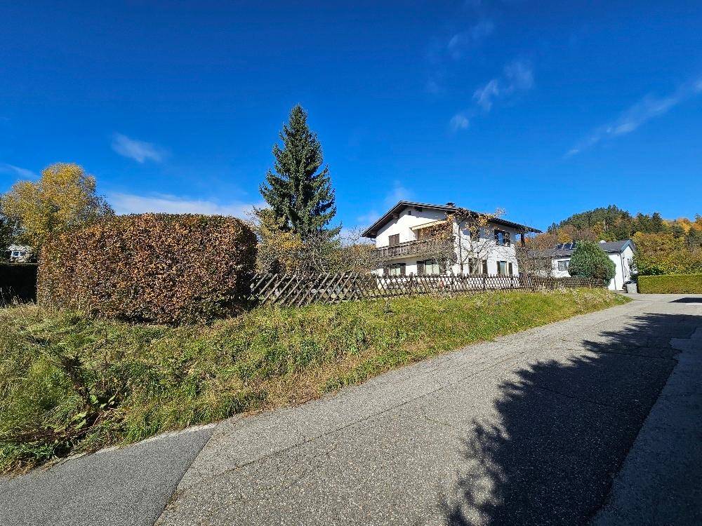 Ländliche Straße mit Blick auf das Haus in der Ferne, umgeben von Hecken und Bäumen.