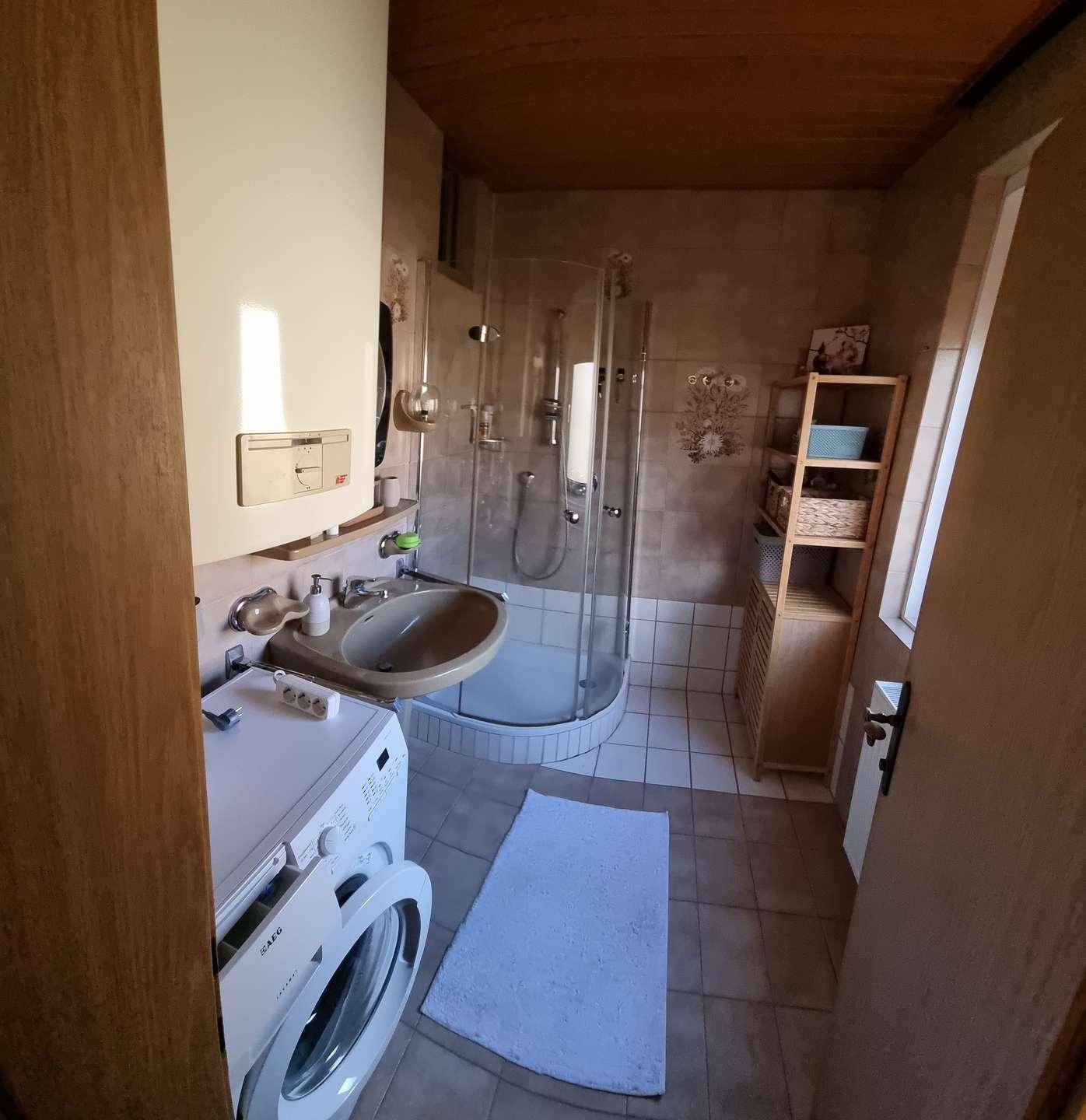 Funktionales Badezimmer mit Duschkabine, Waschbecken, WC und einer Waschmaschine unter der Dachschräge.