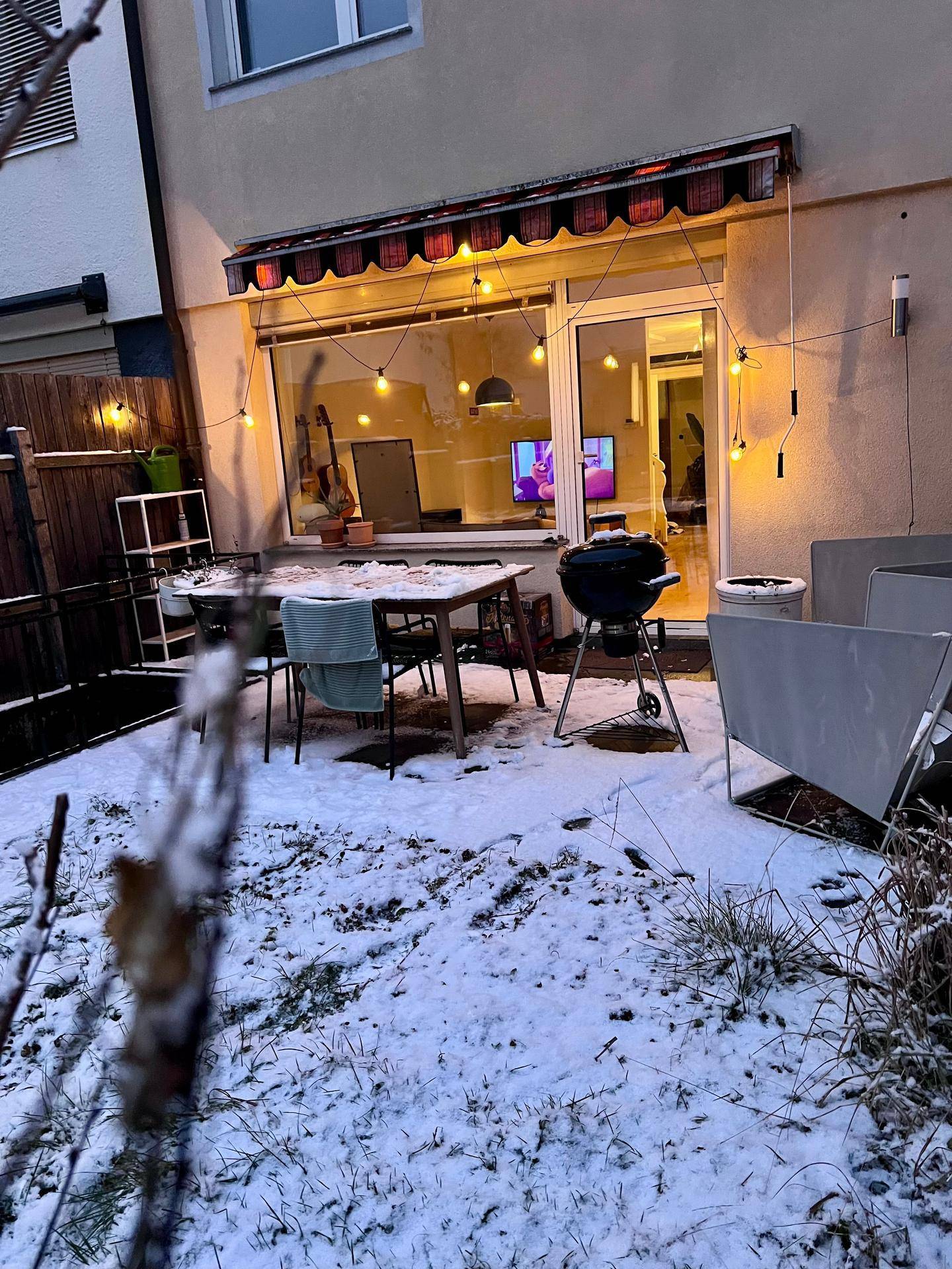 Winterlicher Garten mit Außensitzbereich, Grill und Lichterkette für gemütliche Abende.
