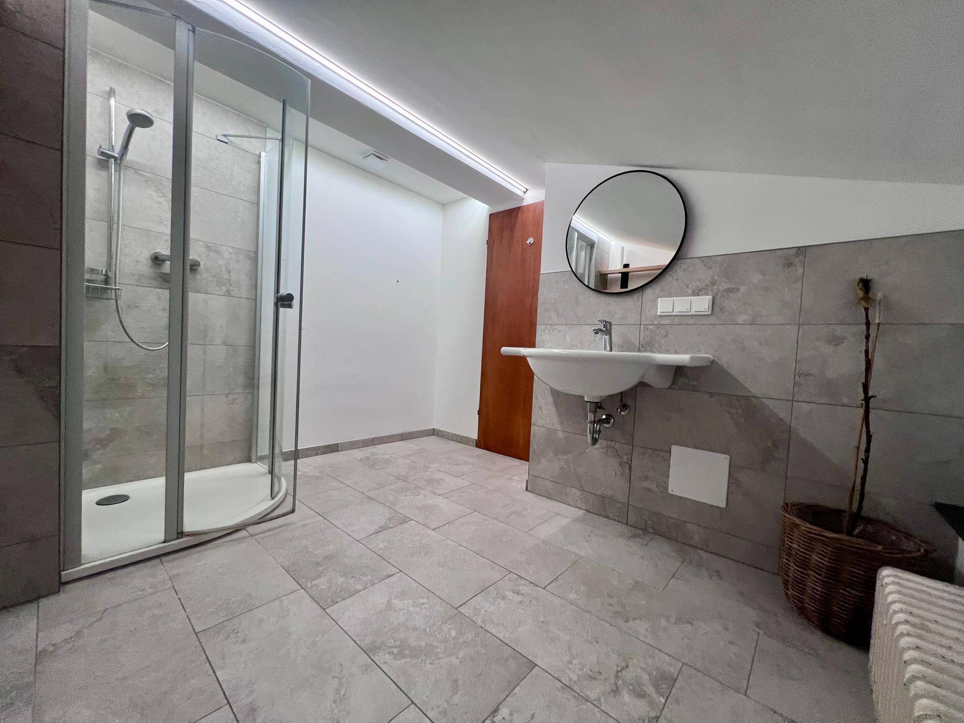 Modernes Badezimmer mit großer Duschkabine, Waschbecken und grauen Fliesen.