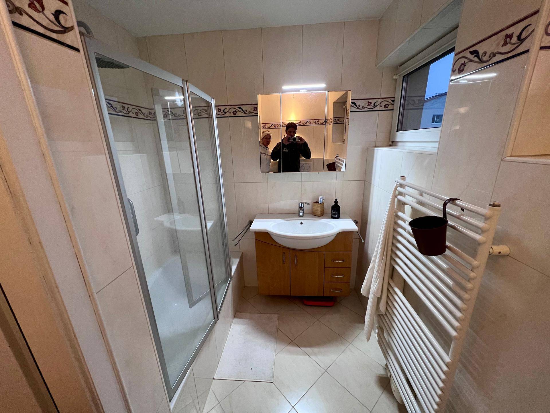 Badezimmer mit Duschkabine, Waschbecken, Spiegelschrank und beheiztem Handtuchhalter.