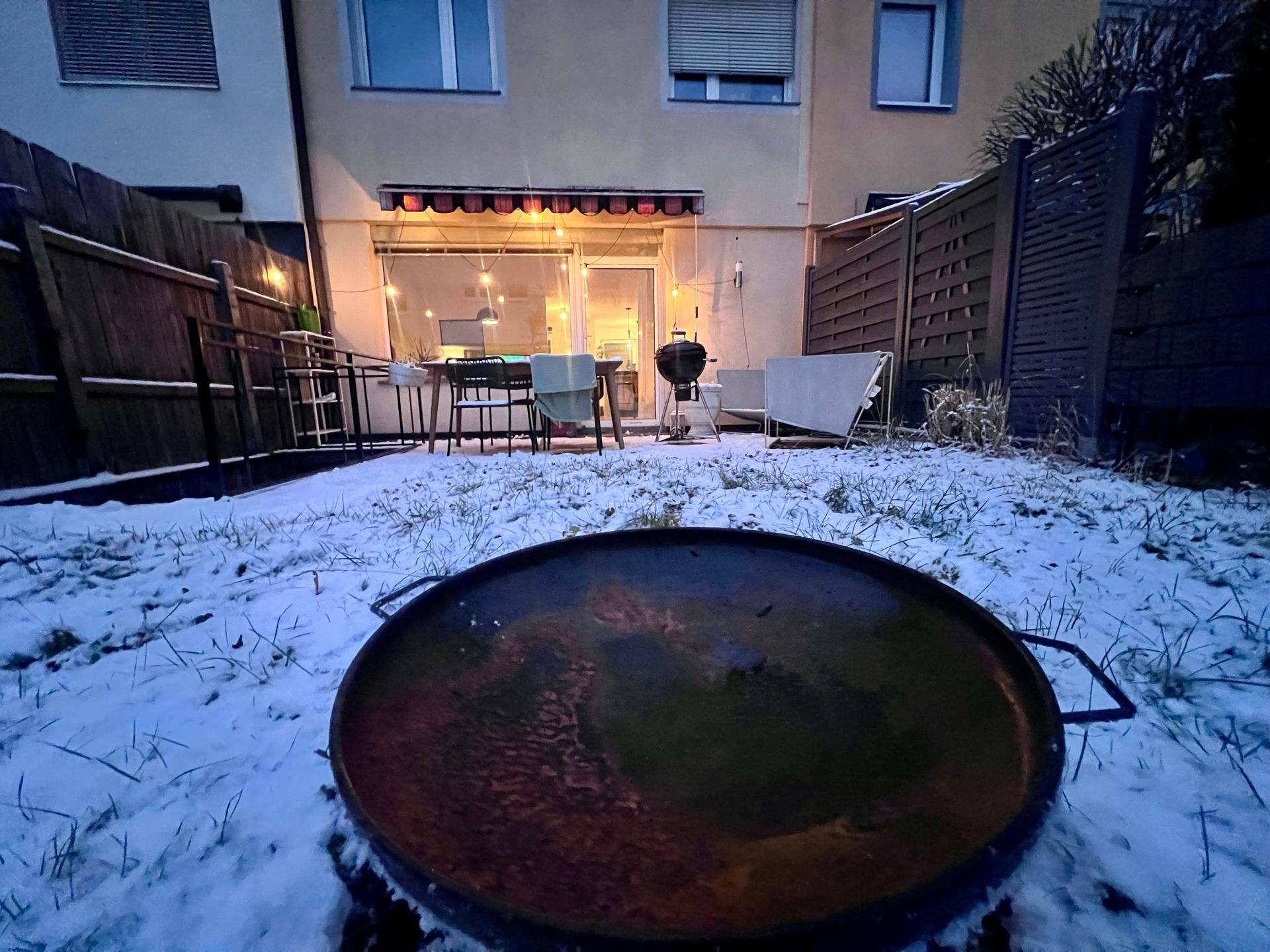 Weitläufiger, schneebedeckter Garten mit Feuerstelle und Blick auf die Gebäudefassade.