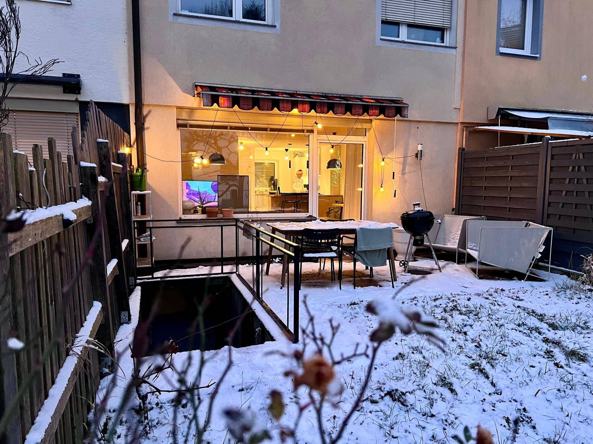 Gartenbereich im Winter mit Terrasse, Außensitzmöbeln und Blick auf das Gebäude.