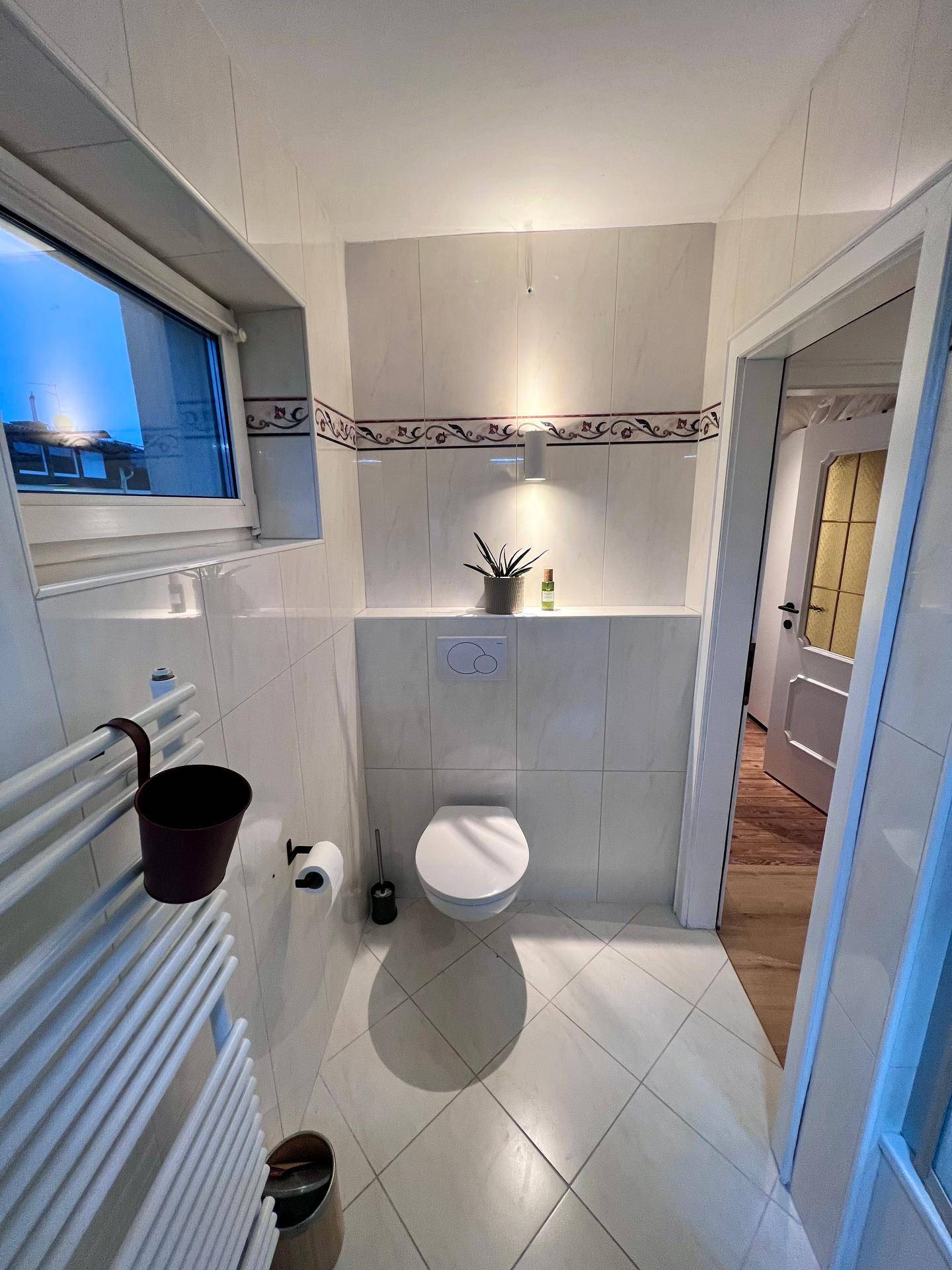 Kleines Gäste-WC mit Wand-WC, Fenster und beheiztem Handtuchhalter.