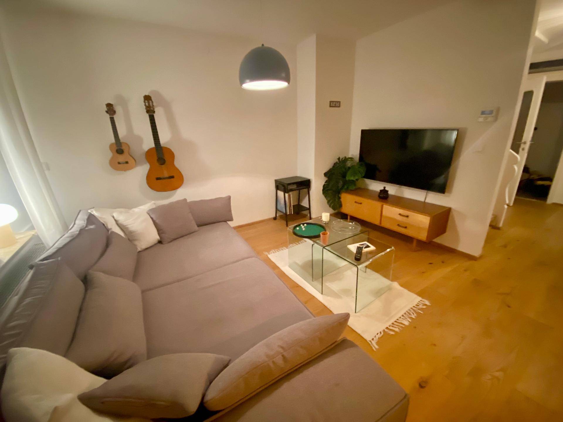 Gemütliches Wohnzimmer mit großem Ecksofa, Holzboden und Wanddekoration in modernem Ambiente.