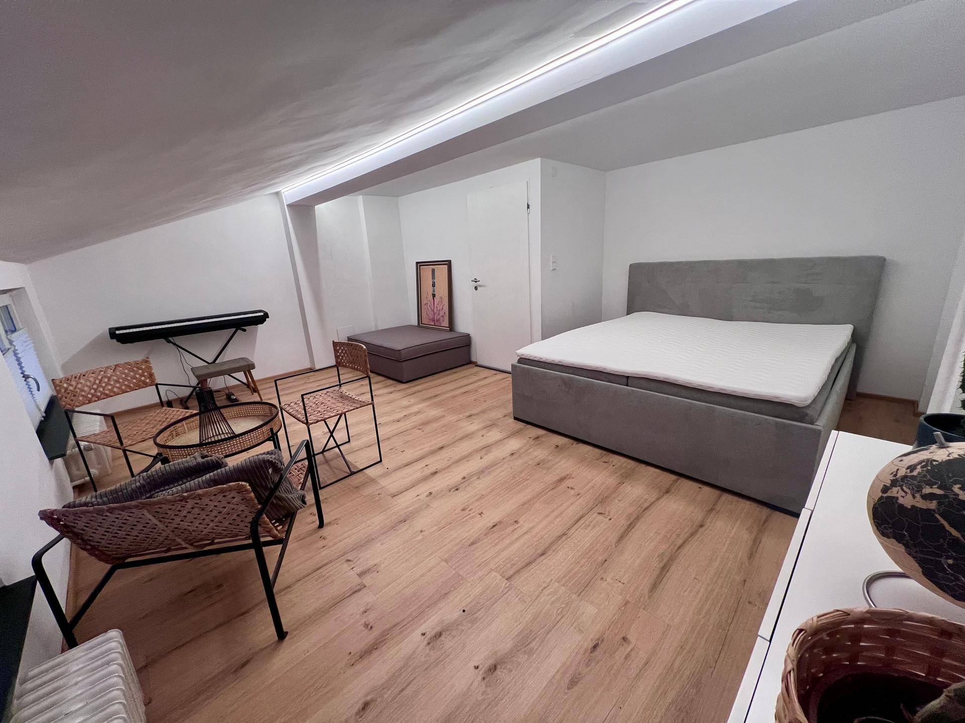 Helles Schlafzimmer im Dachgeschoss mit Doppelbett, Holzboden und Musikinstrument.