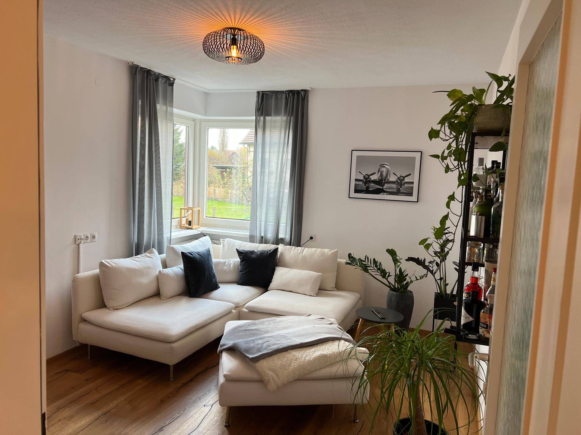 Gemütliches Wohnzimmer mit weißem Ecksofa, Erkerfenster und Blick ins Grüne.