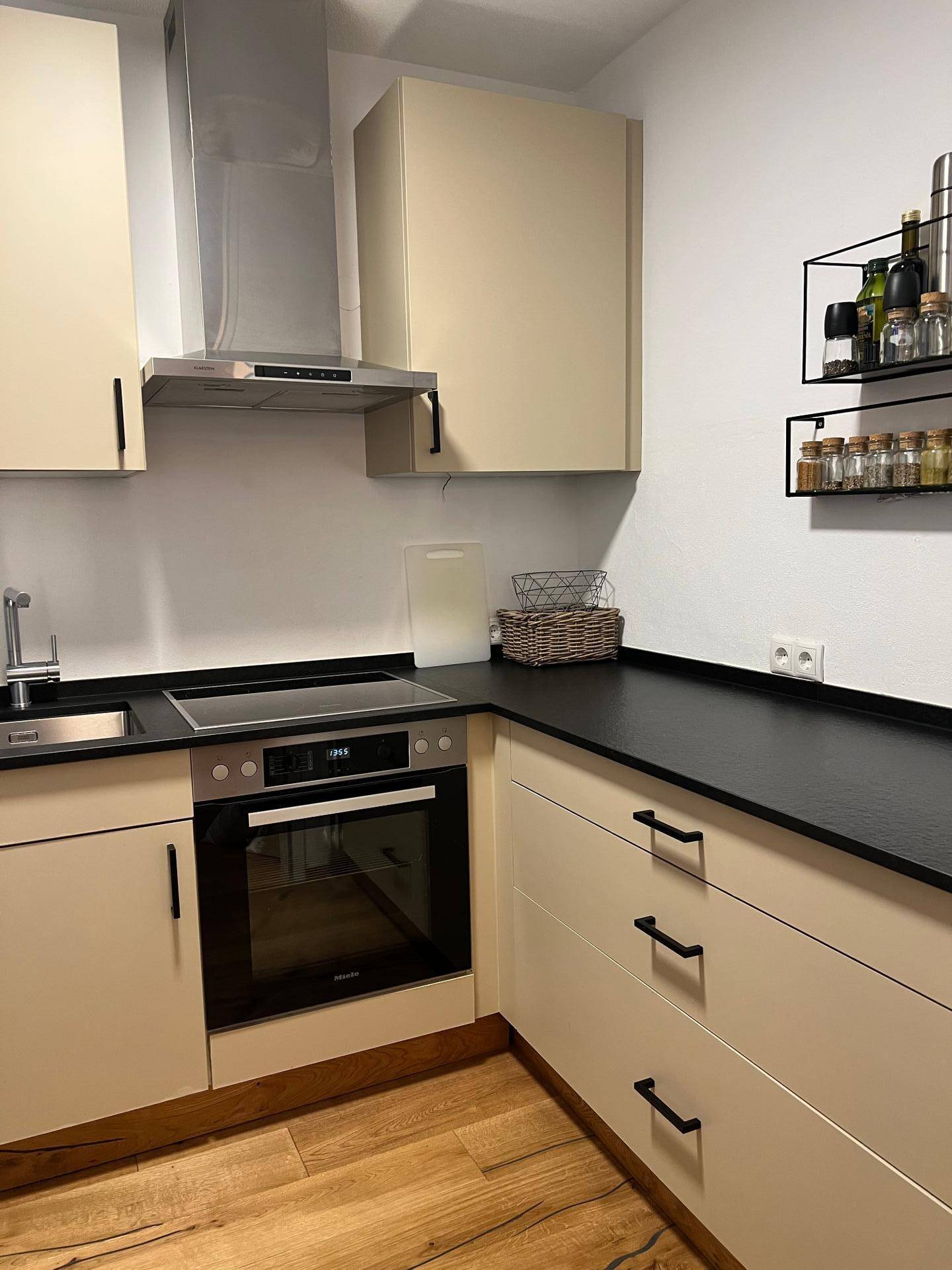 Moderne Küche mit beigen Schränken, schwarzer Arbeitsplatte und integriertem Backofen.
