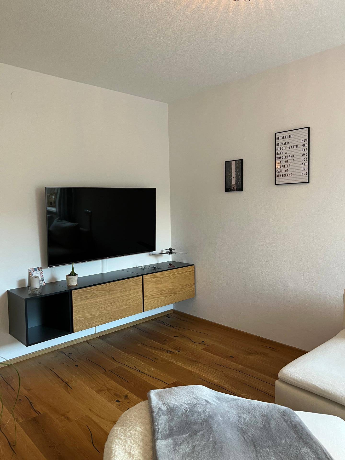 Wohnzimmerwand mit wandmontiertem Fernseher und schwebendem Medienmöbel über Holzboden.