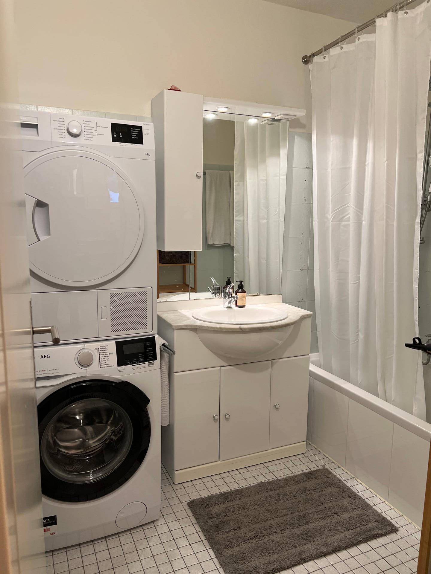 Badezimmer mit Badewanne, Waschbecken, Spiegelschrank und gestapelter Waschmaschine und Trockner.
