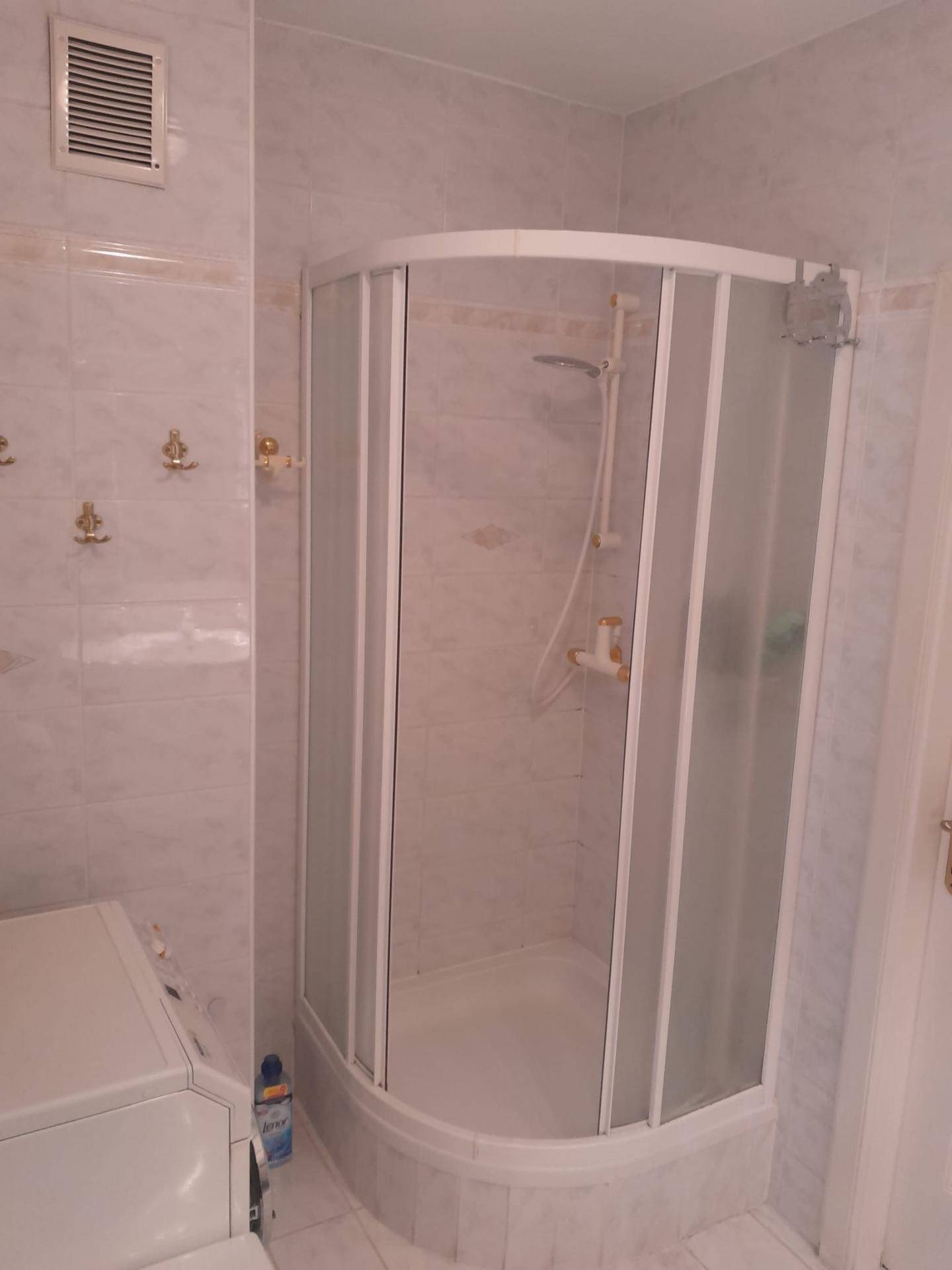 Badezimmer mit einer Eckduschkabine und einer Waschmaschine, umgeben von hellen Fliesen.
