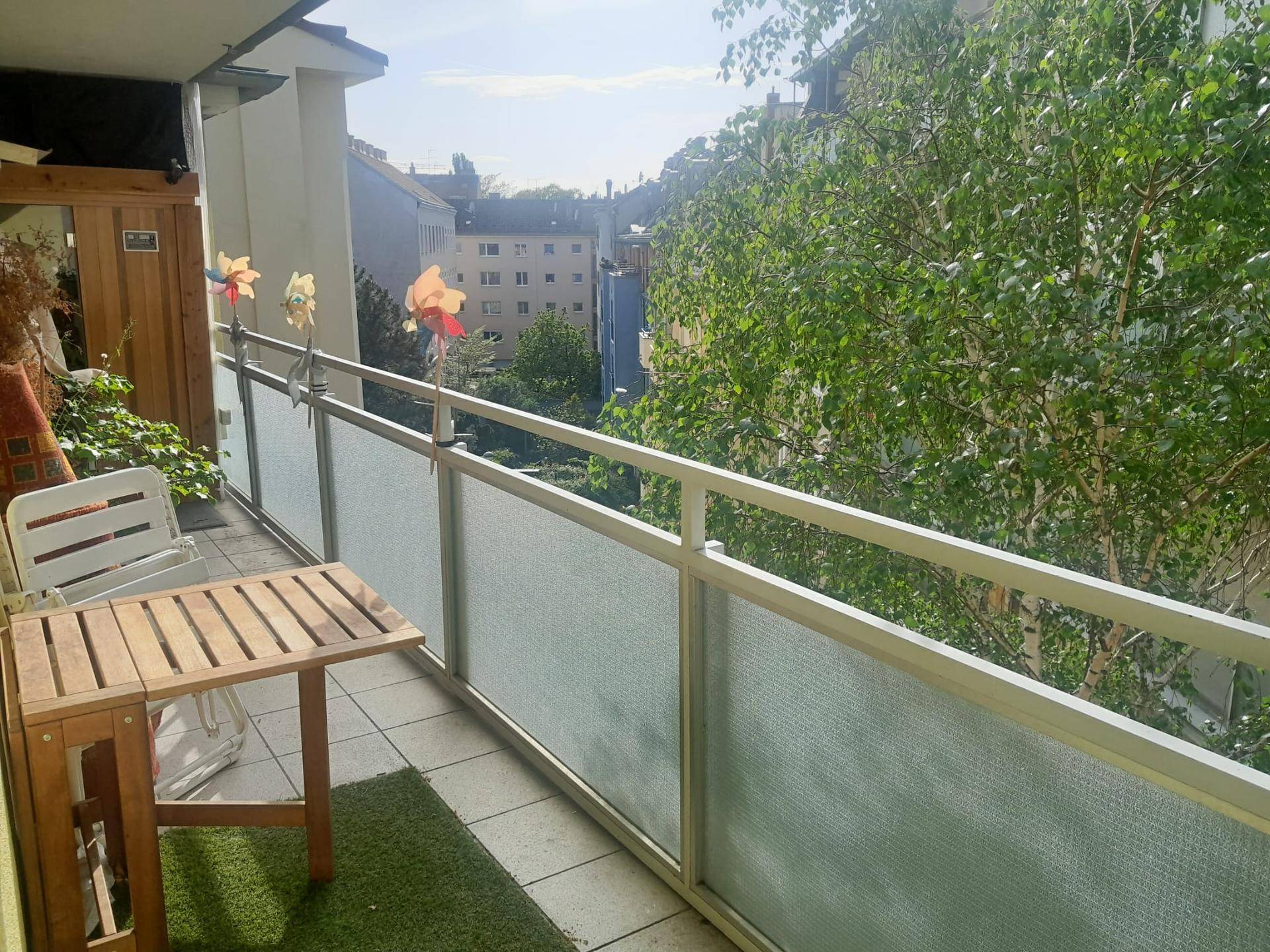 Gemütlicher Balkon mit Sitzgelegenheiten und Blick ins Grüne sowie auf die umliegenden Gebäude.