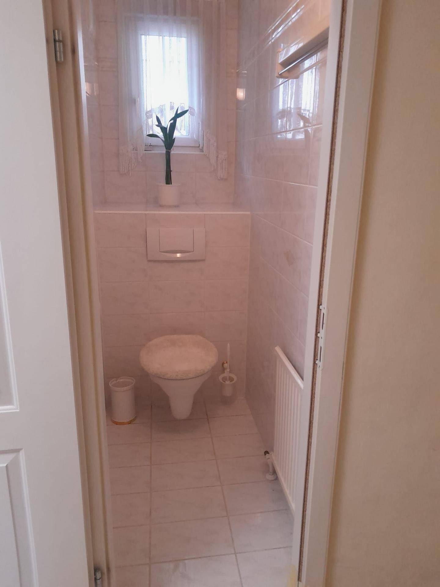 Separates WC mit wandhängender Toilette und einem kleinen Fenster für natürliche Belüftung.