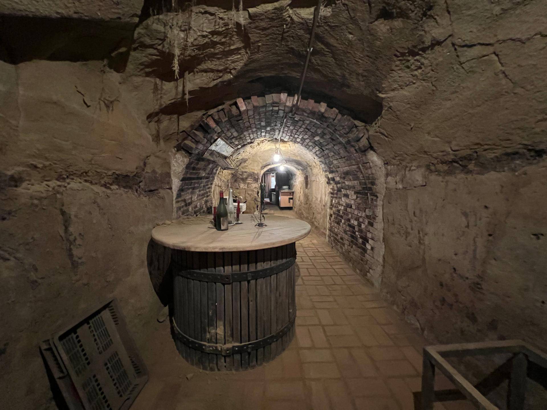 Historischer Weinkeller mit einem großen Holzfass als Tisch und Ziegelgewölbe im Hintergrund.