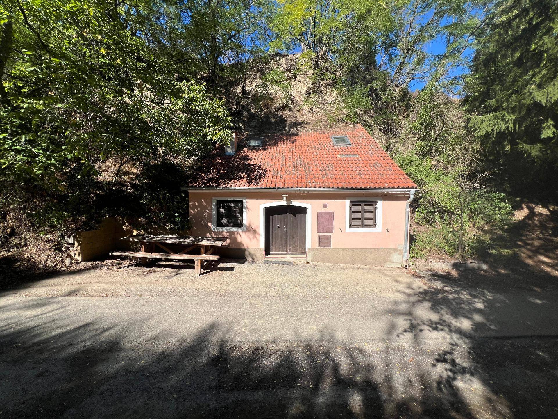 Traditionelles Haus mit rotem Ziegeldach und Dachfenster, umgeben von üppigem Grün und einem Schotterweg.